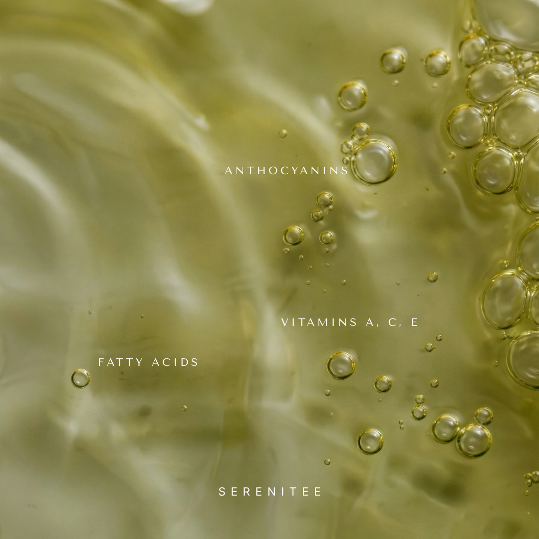 A drop of emerald green Serenitee face oil on skin, showcasing the lightweight, non-comedogenic texture powered by oil-dispersed Hyaluronic Acid.