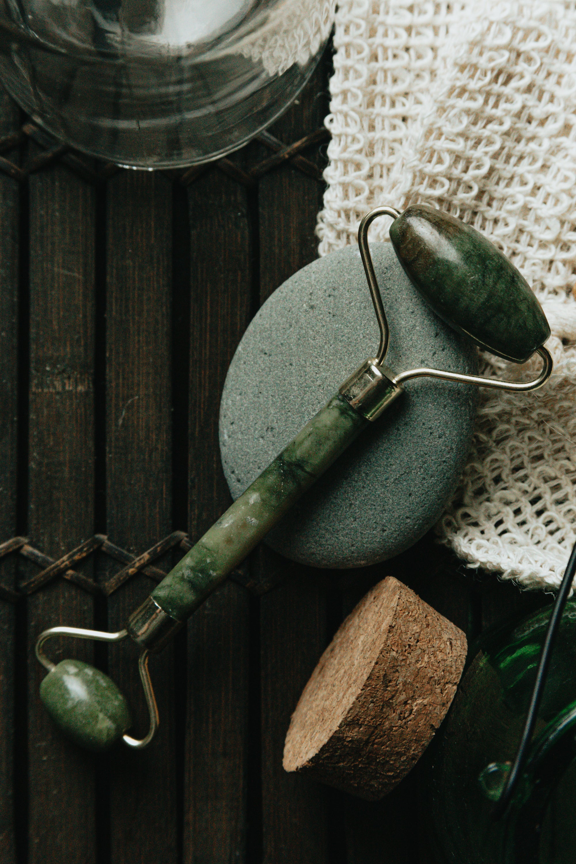 Jade facial roller on a smooth stone beside textured cloth.