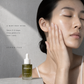 Woman gently pressing Serenitee Blue Tansy Antioxidant Face Oil into her cheek as part of a daily skincare ritual.