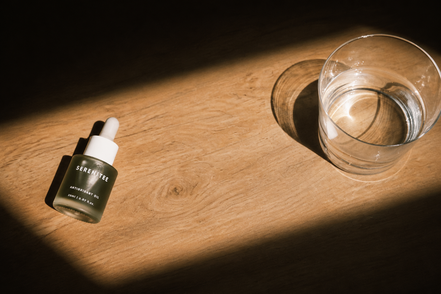 Serenitee Antioxidant Oil beside a glass on a wooden surface
